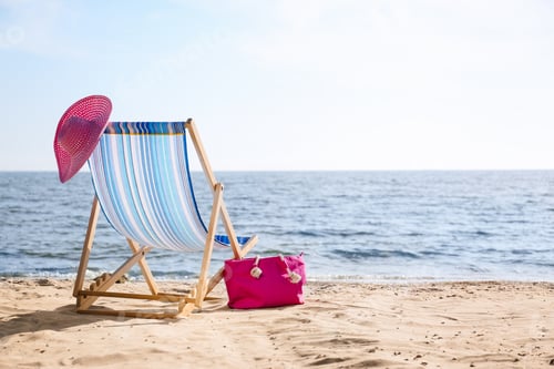 Preview: Lounger, hat and bag on sand near sea, space for text. Beach objects
