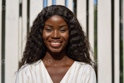 Preview: Happy smiling young black African woman posing outdoors for portrait.