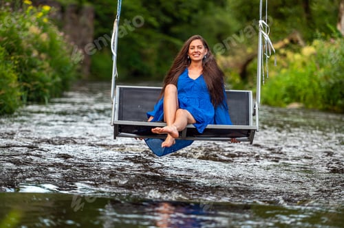 Preview: a joyful young woman swings on a rope swing across a fast-flowing river