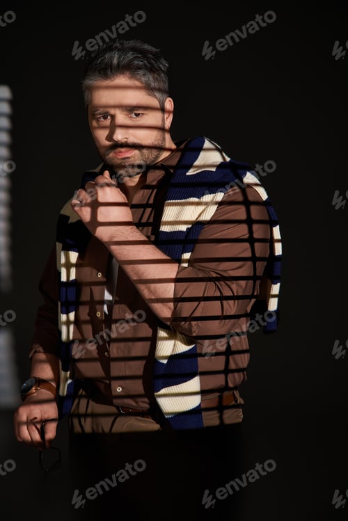 Preview: Stylish man with bristle exudes confidence in studio setting with artistic shadows