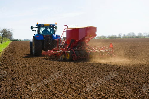 Preview: Farm tractor and seed drill sowing ploughed field in spring