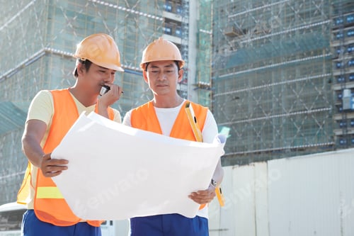 Preview: Contractor talking with builders via walkie-talkie when looking at building plan with head engineer