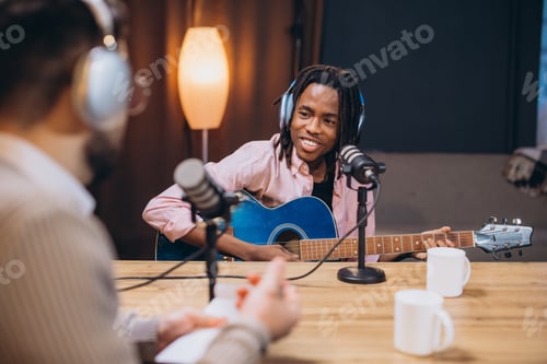 Preview: Young musician playing guitar and singing during a podcast interview in a recording studio