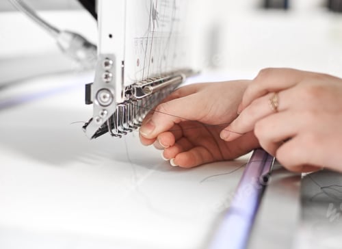 Preview: Close-up of woman hands filling thread in modern embroidery machine on white copy space background.