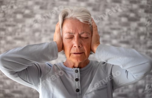 Preview: Desperate frustrated senior woman in pain with hands on ears, sitting at home alone
