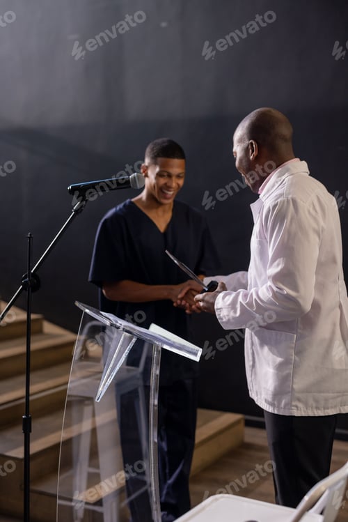 Preview: Man receiving award on stage, smiling and shaking hands with presenter