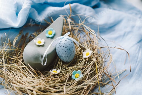 Preview: Colorful Easter eggs nestled in a nest surrounded by flowers and straw on a light blue background