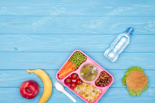 Preview: top view of tray with kids lunch for school, bottle of water and fruits on blue wooden surface