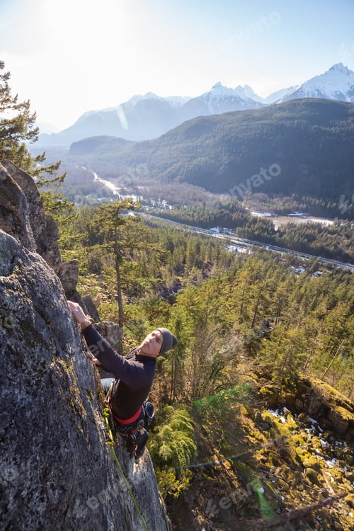 Preview: Male Rock climber climbing on the edge of the cliff during a sunny winter sunset