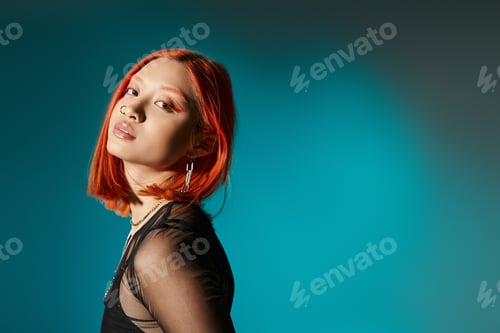 Preview: portrait of pierced asian woman with bold eye makeup looking at camera on blue background
