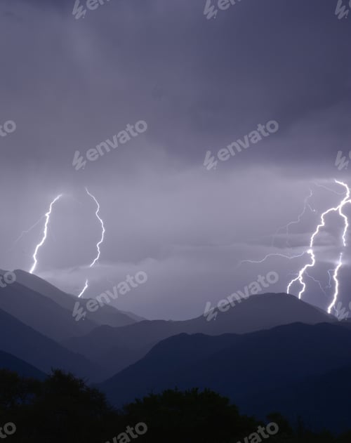 Preview: Stormy evening in the mountains with bright flashes of lightning giving the cloudy sky a purple glow