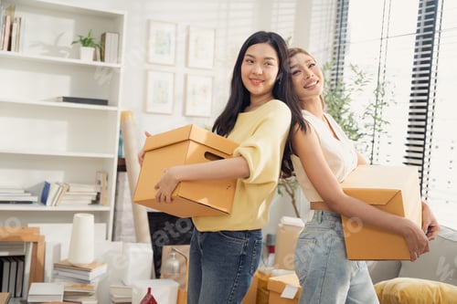 Preview: Happy Asian girl friends holding cardboard boxes moving to the new home.