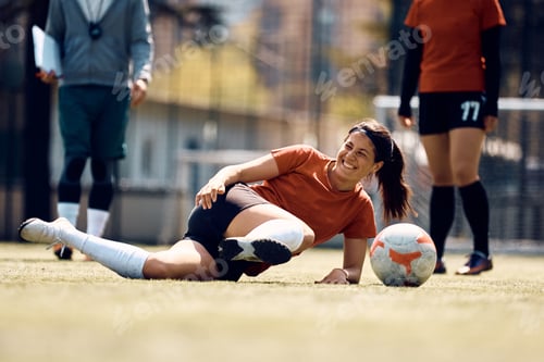 Preview: Happy athletic woman laughing after slipping on the grass during soccer training.