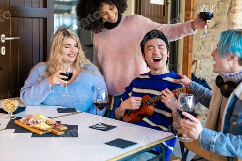 Preview: International group of friends sitting at a table in an outdoor pub having fun and singing