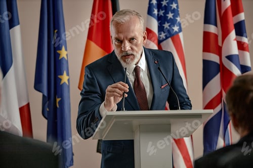 Preview: Senior Caucasian Man Delivering Speech at Podium during International Conference