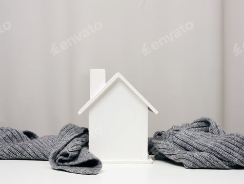 Preview: White wooden miniature house wrapped in a gray knitted scarf