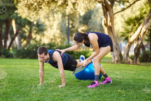 Preview: Personal trainer assisting man doing plank exercise with stability ball