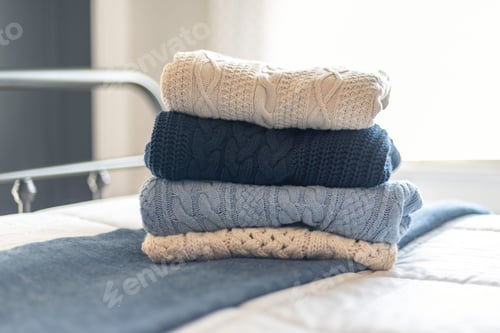 Preview: Stack of Folded Knitted Sweaters on Bed