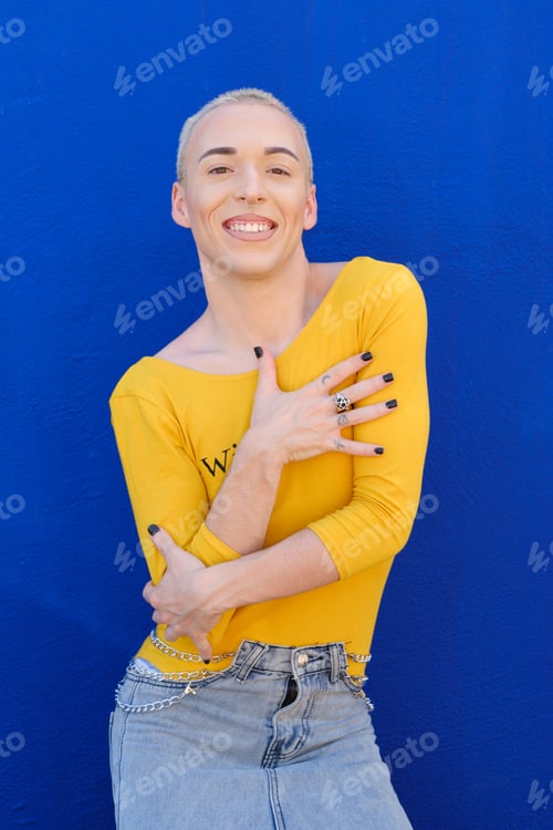 Preview: Young non-binary person looking at the camera and smile while posing outdoors over blue background