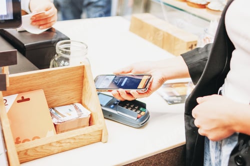 Preview: Young woman with mobile phone in her hands pays for order at checkout in shop