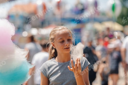 Preview: Girl eating cotton candy at amusement park on summer day