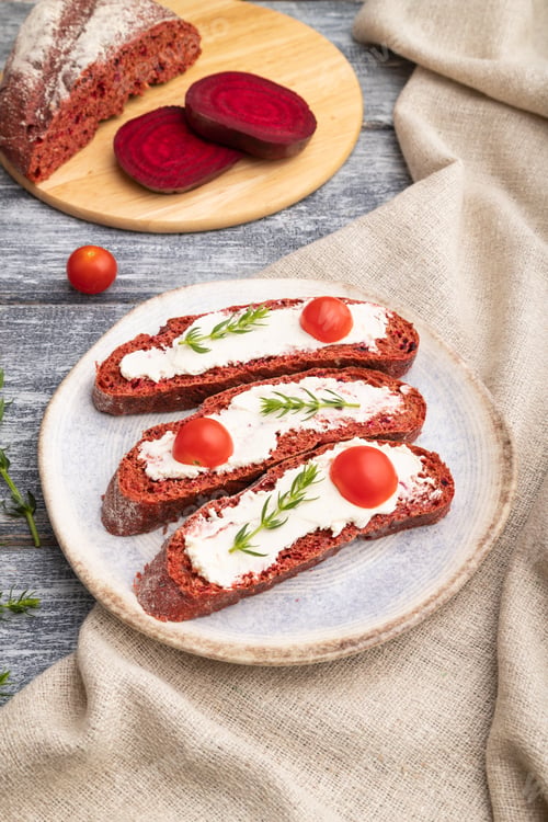 Preview: Red beet bread sandwiches with cream cheese and tomatoes on gray wooden background. Side view.