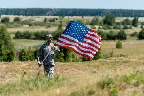 Preview: selective focus of handsome military man in uniform and cap holding american flag