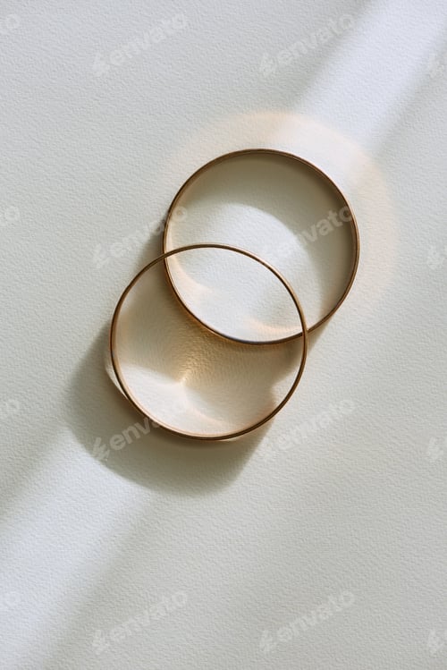 Preview: top view of two beautiful golden rings on white surface with sunlight