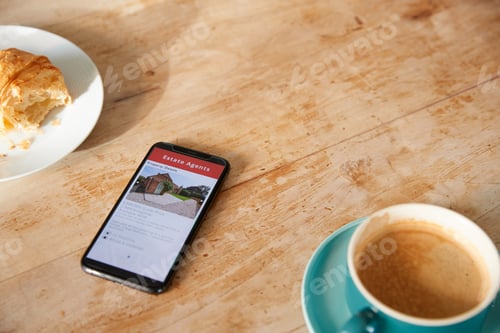 Preview: Close Up Of Mobile Phone With Realtors Property App Lying On Café Table