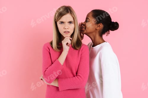 Preview: Black girl smiling while whispering secret to displeased friend