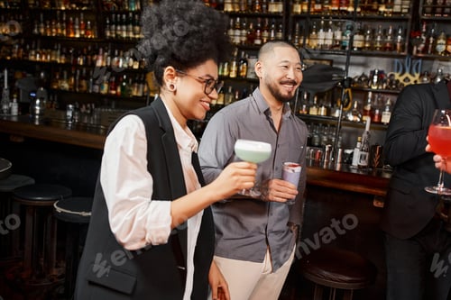 Preview: asian man and african american woman holding cocktails and smiling during after work party in bar