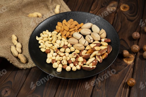 Preview: Mixture of nuts in a black plate on a brown wooden background.