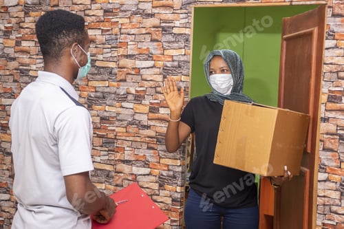 Preview: Courier delivering a package to an African female customer, both wearing a face mask