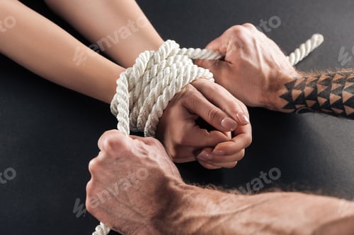 Preview: cropped view of male hands with tattoo tying rope on female hands