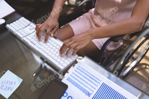 Preview: Mid-section of young disabled mixed-race businesswoman working on computer at desk in the office