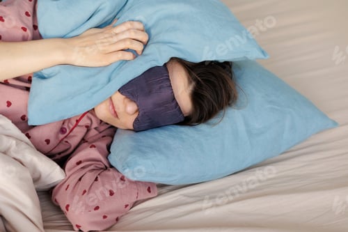 Preview: young woman in bed wakes up, insomnia, sleep disorder. person in sleep mask holds onto pillows