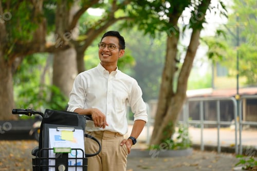Preview: Confident young businessman looking away standing near his bicycle in urban park