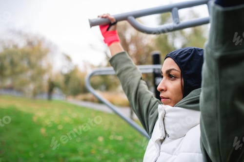 Preview: Young muslim woman in sports hijab doing work out in outdoor training ground.
