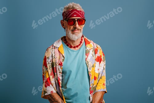 Preview: Hipster senior man in stylish shirt and bandana looking at camera against blue background