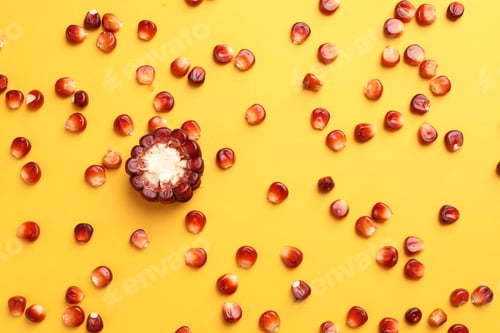 Preview: Piece of ripe red corn cob surrounded by kernels on yellow background, flat lay