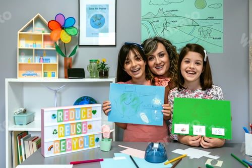 Preview: Teacher in classroom looking at camera next to students showing colorful ecological drawings