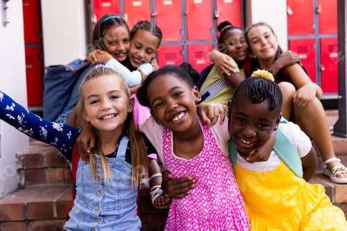 Preview: Portrait of diverse happy schoolgirls embracing in elementary school cloakroom