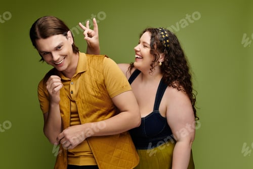 Preview: Young plus size woman playfully posing with her male friend against a vibrant green background
