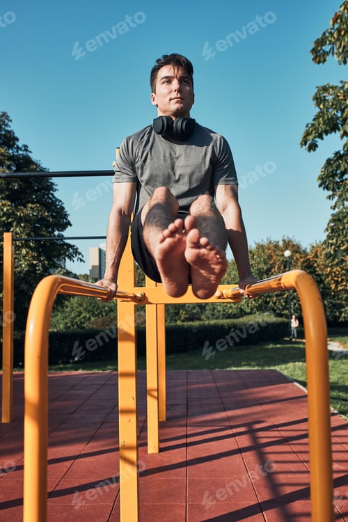 Preview: Young man doing L-Sit on parallel bars during his workout in a modern calisthenics street workout