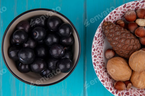 Preview: top view cherry plum in a bowl with fir cones and hazelnuts in a plate on a turquoise background
