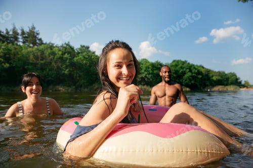 Preview: Happy group of friends having fun, laughting and swimming in river