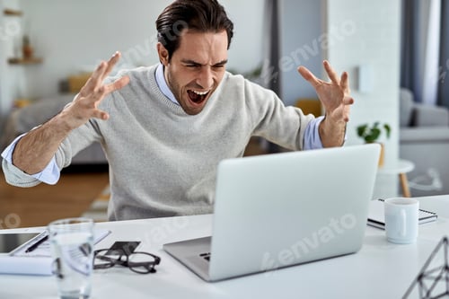 Preview: Frustrated businessman screaming while working on a computer at home.