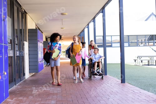 Preview: Diverse group of school children walking in school corridor talking, one in wheelchair, copy space