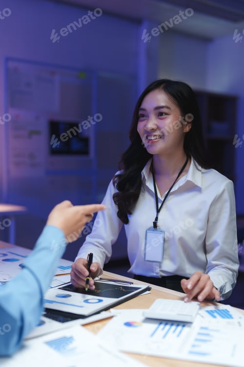 Preview: Businesswoman smiling and discussing charts with colleague in office at night