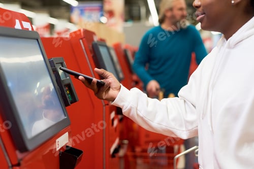 Preview: Young black woman with smartphone making contactless payment by terminal